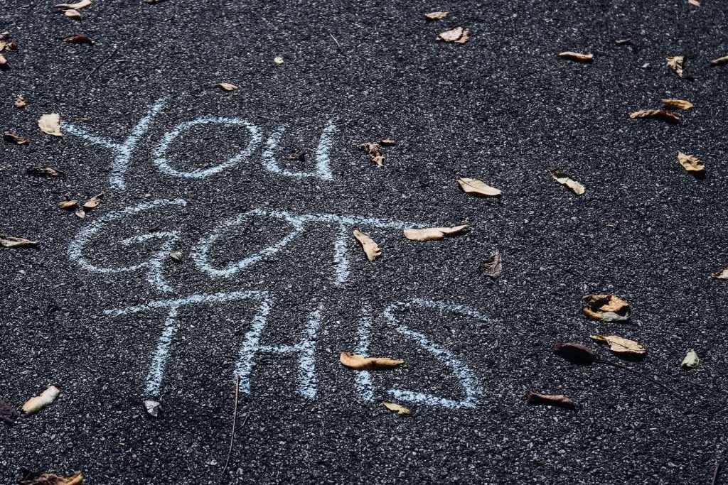 The words YOU GOT THIS written in chalk on a bitumen road with leaves and twigs around it.