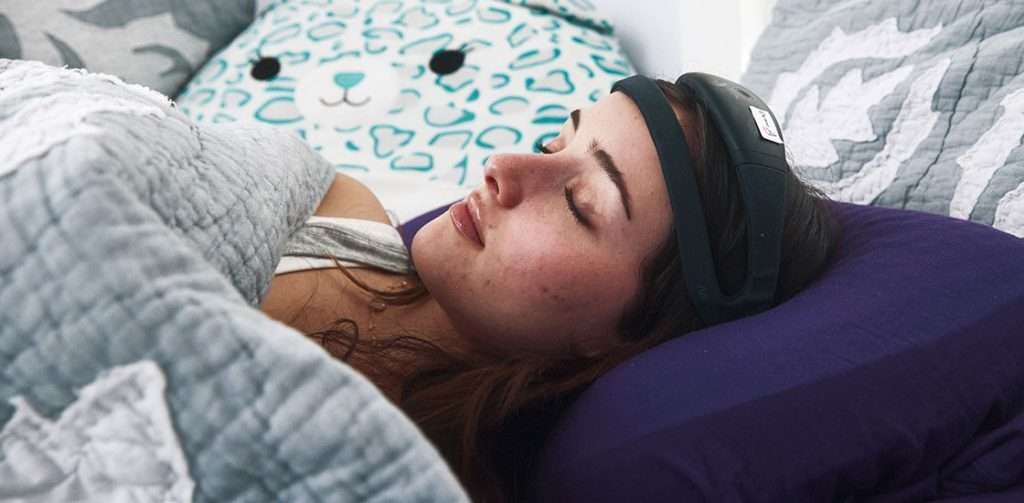 A woman lies in bed sleeping with a home sleep monitoring headband on her forehead.