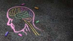Pink chalk head in profile with multicoloured chalk brain on bitumen