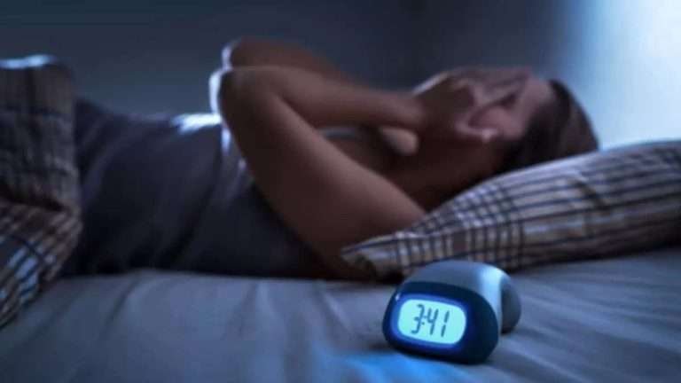 Woman lies in a bed with her hands to her face while the digital clock in the foreground reads: 3:41