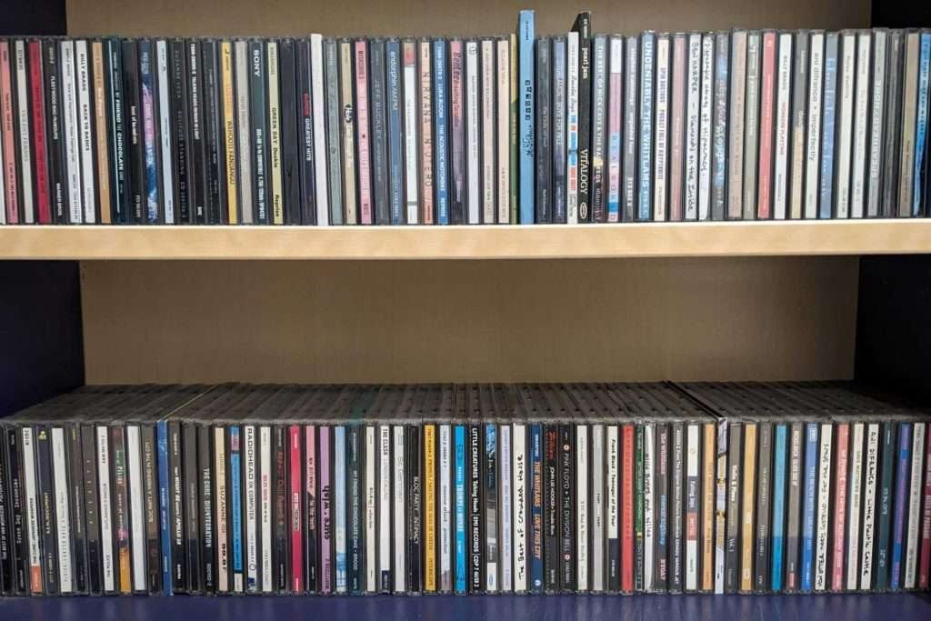 Two rows of CDs standing like books on shelves, in a blue bookcase.
