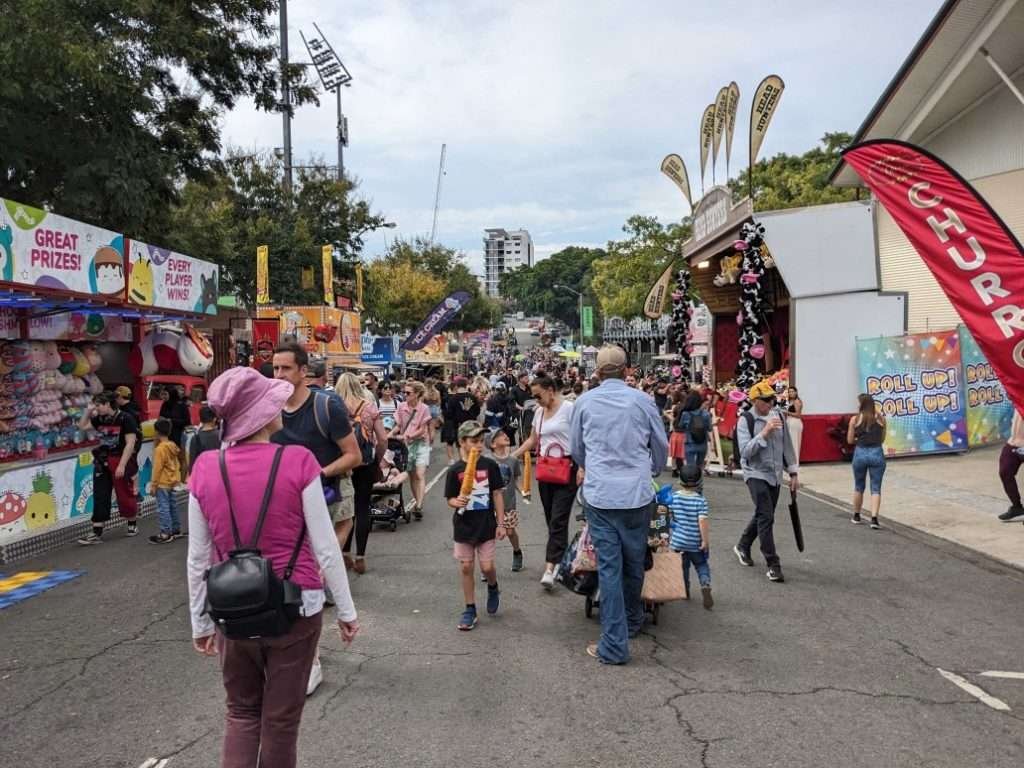 Glenn's wife with her back to the camera, standing before the Ekka crowds, sideshow amusements lining the street.