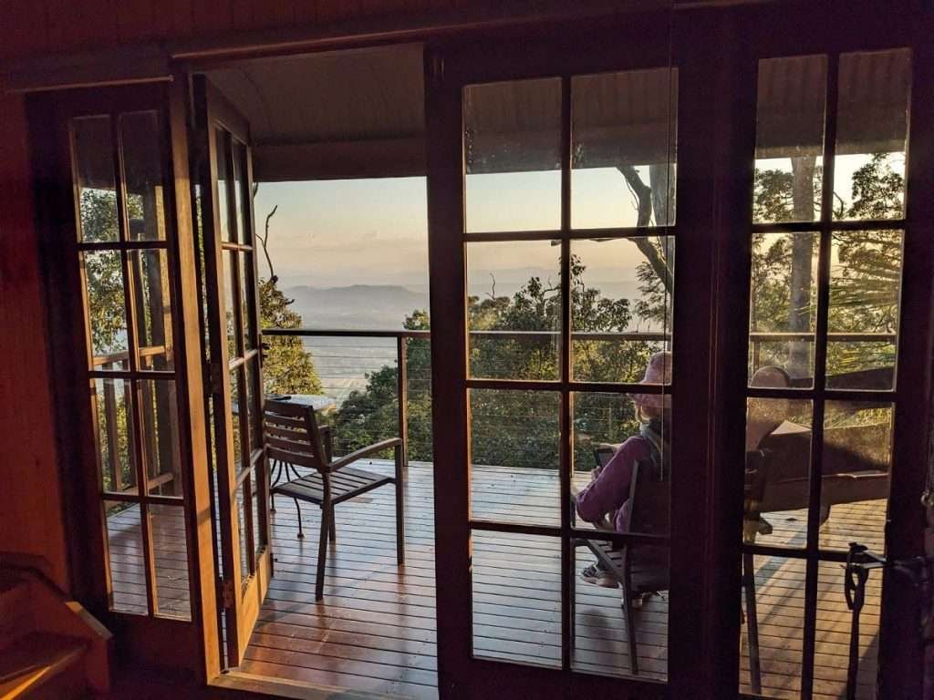 The view through french doors of a person sitting on a deck overlooking a view across the mountains to the horizon