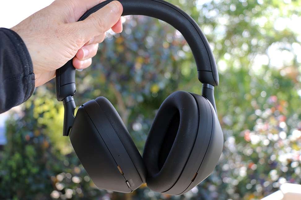 Hand holding a pair of black Sony XM5 over-ear headphones