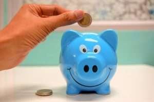 Hand putting a coin into a blue piggy bank adorned with a large smile